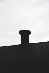 A close view of metal flashing directing rainwater around a chimney on a shingled roof.