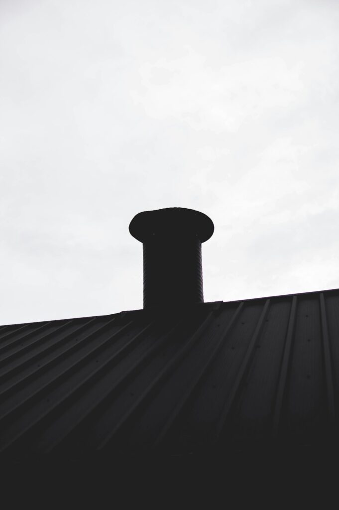 A close view of metal flashing directing rainwater around a chimney on a shingled roof.