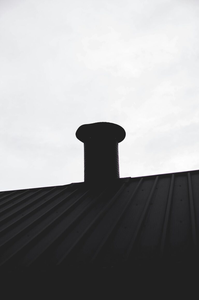 A close view of metal flashing directing rainwater around a chimney on a shingled roof.