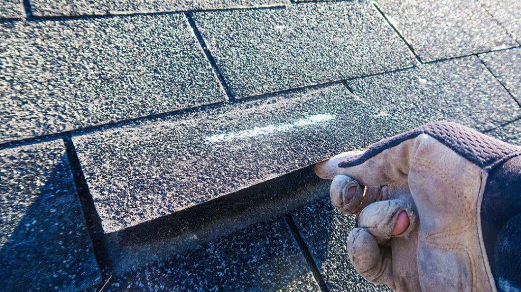 A homeowner views dented shingles and metal flashing from the ground after a hailstorm.