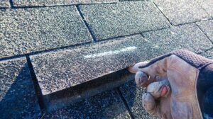 A homeowner views dented shingles and metal flashing from the ground after a hailstorm.